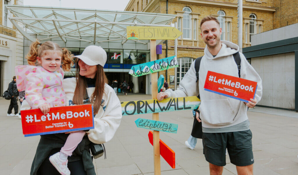 Photo: family holding 'let me book' signs at Kings Cross Station