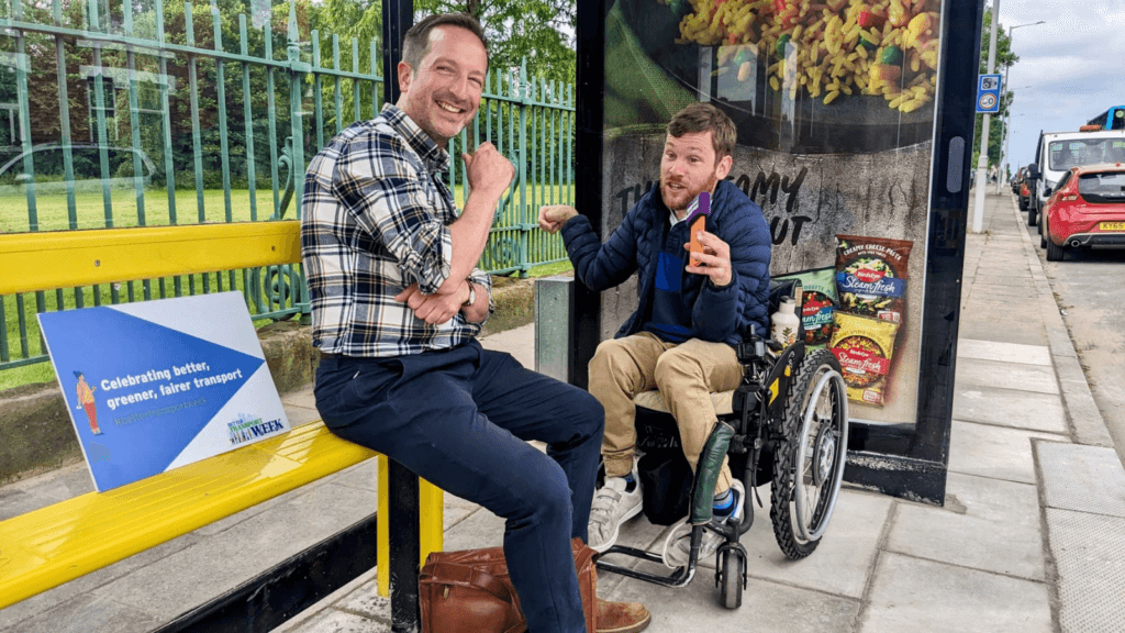 2 men one a wheelchair user at a bus stop