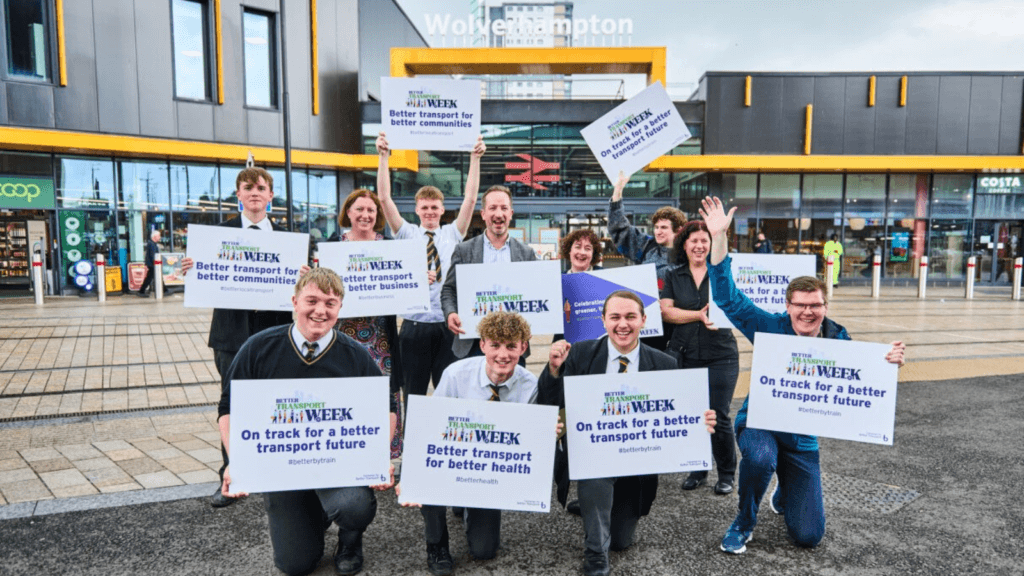 Group of school children in uniforms holding up Better Transport Week signs outside Wolverhampton Railway Station