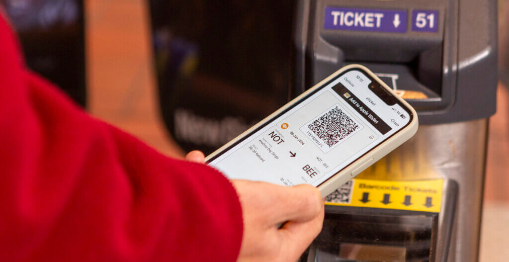Hand holding a phone showing an eticket over an automatic rail ticket barrier