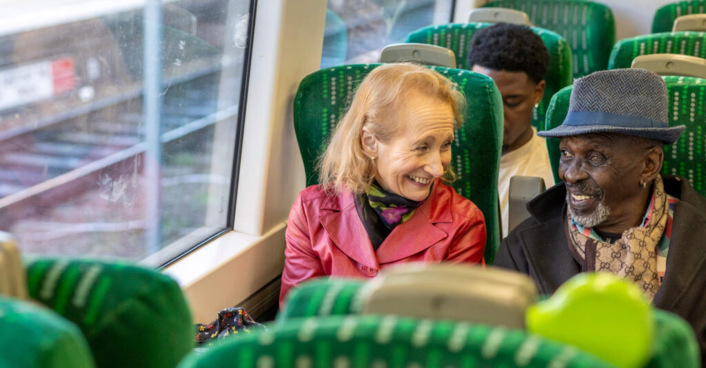 Two people seated next to each other on a train smiling