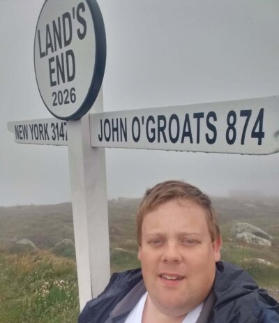 Man standing in front of a sign pointing to John O'Groats and Land's End